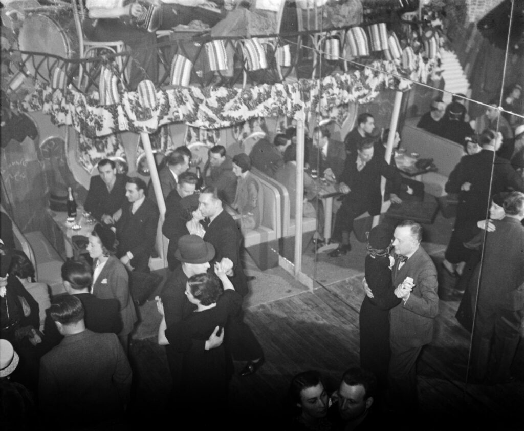 Sala da ballo affollata con coppie in pista e festoni al soffitto, 1936